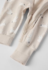 Beige børnebukser med kaninprint, med lynlås, ribbede manchetter og små brune prikker. Blød, strækbar stofstruktur.