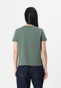 Grön bomullströja med rund hals och korta ärmar, med rak skärning och en slät yta. Bärs ihop med mörkblåjeans.