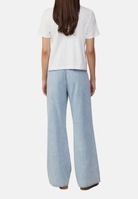 Biała koszulka z krótkim rękawem w połączeniu z jasnoniebieskimi jeansami o szerokich nogawkach, prezentująca luźny krój i gładką fakturę denimu.