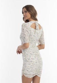 Blumenkleid mit kurzen Puffärmeln, Raffung an den Seiten und einem Schlüsselloch-Rücken. Hergestellt aus leichtem Stoff mit weißem Hintergrund und pastellfarbenen Mustern.