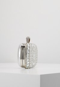 Pochette argentée étincelante avec un travail de perles complexe, un fermoir métallique et des strass décoratifs. Forme rectangulaire compacte avec une texture lisse.