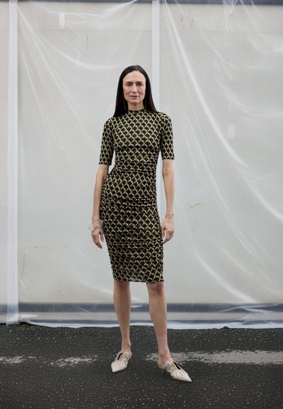 Przylegająca zielona sukienka dzianinowa z geometrycznym wzorem, krótkimi rękawami i marszczeniami. Do tego jasne buty na wsuwki.