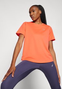 Bright orange athletic t-shirt with short sleeves, smooth texture, and a round neckline. Paired with fitted purple leggings.