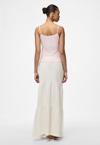 Svetle růžový žebrovaný top na ramínka v kombinaci s krémovou maxi sukní s volány vyrobenou z texturované tkaniny, která má tenké ramínka a uvolněný střih.