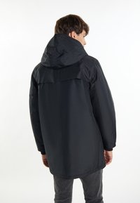 Giacca nera impermeabile con cappuccio, caratterizzata da un esterno liscio, una vestibilità ampia e polsini elasticizzati. Cuciture visibili e design a lunghezza intermedia.
