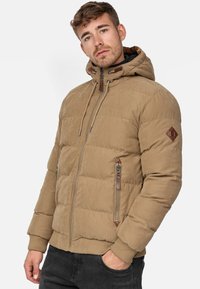 Chaqueta acolchada beige con capucha, diseño acolchado, cremalleras laterales y detalles en cuero marrón. Puños y dobladillo acanalados para mayor calidez.