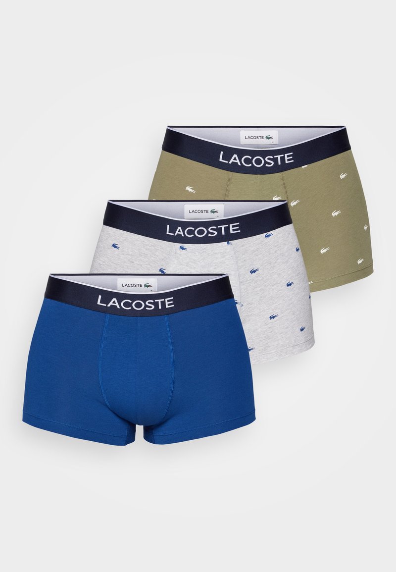 Trzy pary bokserek Lacoste: jedna niebieska, jedna szara z małymi niebieskimi logotypami i jedna oliwkowa z podobnymi akcentami. Pasek z materiału w kolorze granatowym.