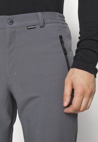 Szare spodnie wykonane z elastycznego materiału o gładkiej teksturze, z zamykaną na zamek kieszenią, zapięciem na guzik oraz elastycznym paskiem w talii.