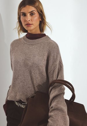 Vaalea ruskea, oversized villapaita, jossa on ribbauscrew-kaarroke. Yhdistetty tummanruskeaan anteeksiin laukkuun ja burgundin väriseen korkeakauluspaidasta sen alla.