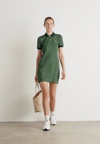 Rochie polo verde cu un model, guler, mâneci scurte și slituri laterale; asortată cu o geantă tote bej și teniși albi.