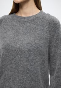 Szürke gyapjú pulóver kerek nyakkivágással, lágy textúrával és egyszerű dizájnnal. Raglán ujjas és laza szabású.