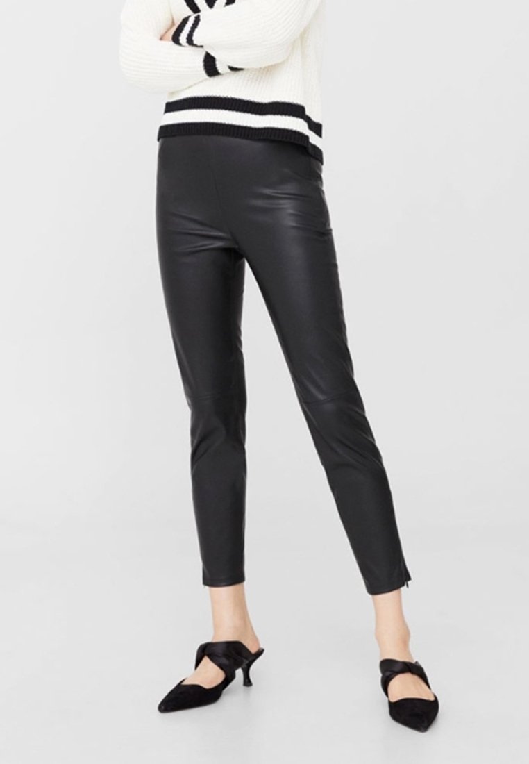 Osoba ubrana w czarne spodnie z sztucznej skóry, kremowy sweter w czarne paski oraz czarne szpilki z zakrzywionymi paskami.