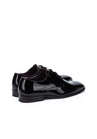 Oxfords de charol negro con un acabado liso y brillante, punta redondeada, diseño de cordones y tacón bajo. El interior tiene un color contrastante.