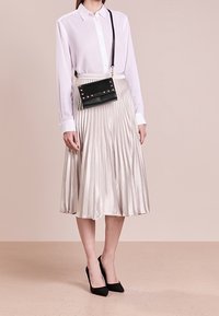 Biała koszula z długim rękawem zapinana na guziki, metaliczna plisowana srebrna spódnica, czarna torebka na ramię z ćwiekami oraz czarne szpilki.