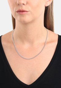 Silberne Kettenhalskette, flaches Design, glatte Textur, mit ineinandergreifenden Gliedern, getragen an einem nackten Hals, kontrastiert mit einem schwarzen V-Ausschnittshirt.