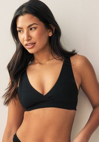 Sort ribstrikket bralette med V-formet halsudskæring, brede stropper og sømløst design. Glat tekstur uden pynt eller mønstre.
