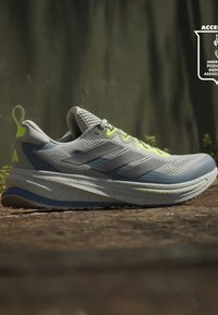 Chaussure de course gris clair avec des touches jaune néon, empeigne en maille respirante et semelle amortie tachetée sur une surface extérieure texturée.