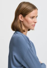 Ljusblå rippad stickad tröja med en texturerad yta, med långa ärmar och en avslappnad passform, presenterad mot en neutral bakgrund.