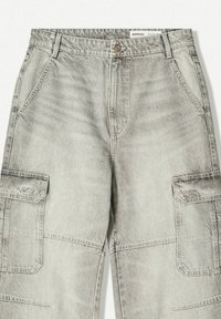 Izblijedjeli sivi cargo traperice s prednjim džepovima, zatvaranjem na dugme i preklopnim džepovima na oba bedra, označene markom Bershka.