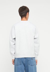Hanorac gri cu mâneci lungi și decolteu tip crew, realizat dintr-un material moale. Purtați-l cu pantaloni din denim albastru, care au două buzunare la spate.