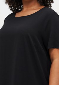 Top negro de manga corta con escote redondo, hecho de tela texturizada. Cuenta con un sutil bolsillo lateral y un corte relajado.