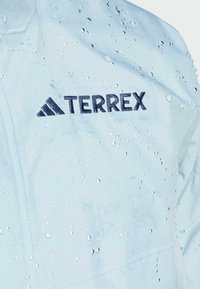 Jasnoniebieska wodoodporna kurtka z kroplami wody, z ciemnoniebieskim logo "TERREX" i gładką, nieteksturalną powierzchnią.