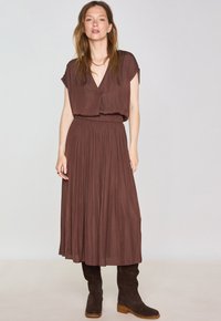 Abito marrone a maniche corte con scollatura a V, vita elastica e gonna plissettata. Stivali marroni in camoscio al ginocchio con tacco a blocco.