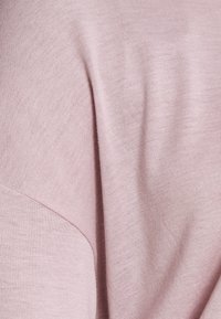 Lichtroze trui met een zachte textuur, een relaxte pasvorm en subtiele ribbelaccenten langs de naden. Glad materiaal met een lichte glans.