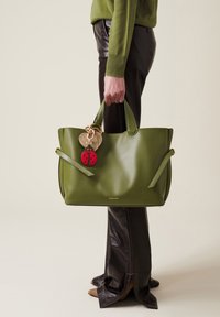 Green leather tote bag with smooth texture, featuring two decorative charms: a woven heart and a red ladybug. Handles attached for easy carrying.