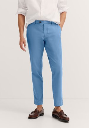 Hellblaue Chinos mit schmalem Schnitt und strukturiertem Stoff. Mit Knopfverschluss und Taschen ausgestattet, kombiniert mit braunen Slippern.