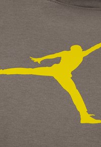 Γκρι βαμβακερό ύφασμα με έντονη κίτρινη σιλουέτα ενός πηδούζοντος ανθρώπου. Υφή με καθαρό, τολμηρό σχέδιο.