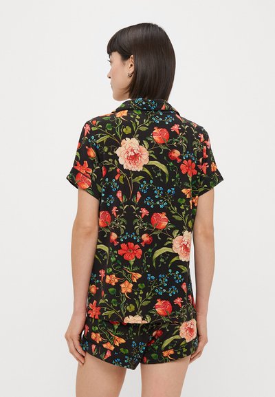 Conjunto de camisa de manga curta e calções com estampado floral, apresentando grandes flores em rosa e vermelho sobre um fundo preto, com acentos em verde e azul.