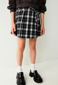 Schwarz-weiß karierten Rock mit Falten, tailliertem Bund und Akzentdetails. Getragen mit schwarzen Loafers und weißen gerippten Socken.