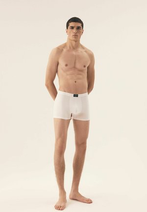White men's boxer briefs with a fitted design, elastic waistband, and smooth texture. Model stands barefoot with a neutral background.
