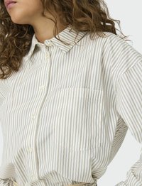 Chemise boutonnée rayée en tissu doux. Présente un col classique, une poche poitrine unique et des rayures verticales en crème et couleurs atténuées.