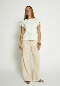 Top bianco a maniche corte con dettagli a bottoni, abbinato a pantaloni beige a gamba larga e scarpe a righe bianche e nere. Texture liscia, design casual.