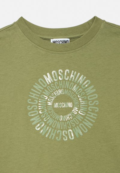 T-shirt vert olive col rond avec texte argenté répété "MOSCHINO" formant des cercles concentriques sur la poitrine.