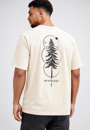 Man wearing cream t-shirt with black graphic of a tall pine tree, circles, a bird, and the word "NEVERLESS" on the back.