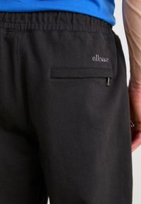 Pantalones de chándal negros con cintura elástica, un pequeño bolsillo con cremallera en la parte posterior y el logotipo "ellesse" bordado en gris.