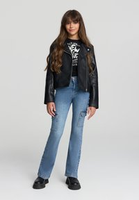 Czarna skórzana kurtka typu cropped na czarnym t-shircie z grafiką, w połączeniu z jasnoniebieskimi spodniami cargo w kantorach i masywnych czarnych butach.