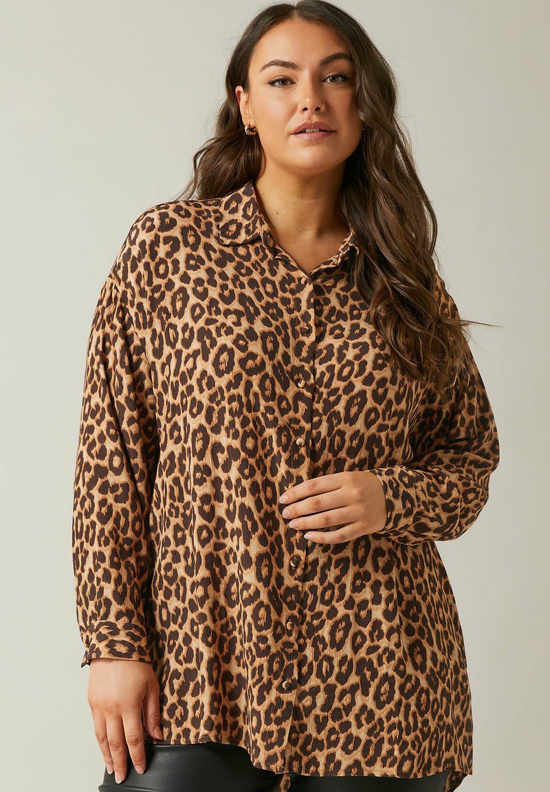 Camisa de manga larga de estampado de leopardo en tonos marrones y beige, con un cierre de botones al frente y un corte relajado con cuello. Textura de tela suave.