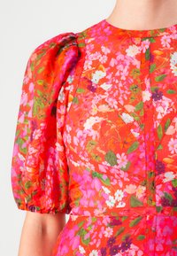 Red floral dress with pink, white, and purple flowers, featuring puffed short sleeves and fitted waist details on a light background.