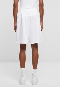 Hvite mesh idrettsshorts med elastisk midje, knelangs design og lett stoffstruktur. Brukt med hvite sko og sokker.