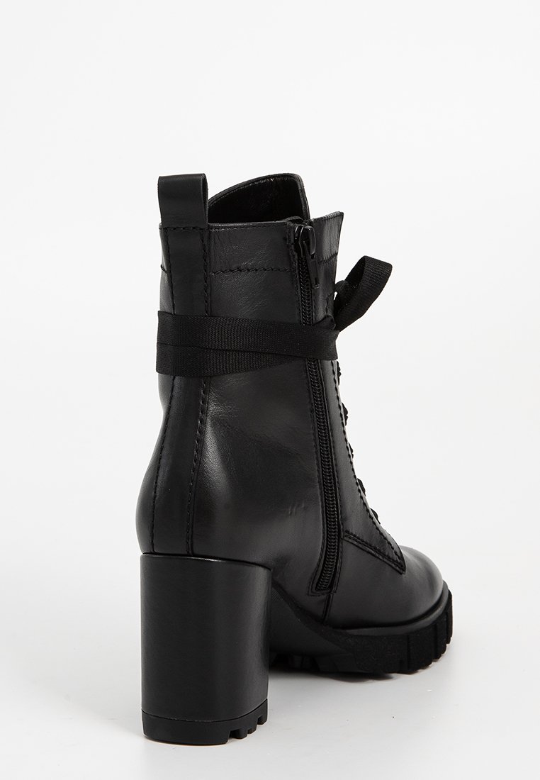 Bottine en cuir noir avec un talon épais, un devant à lacets et une fermeture éclair sur le côté. Caractéristiques d'une semelle texturée et d'une sangle d'accent élastique.