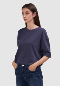 Granatowy, krótki sweatshirt z krótkimi rękawami, wykonany z miękkiego materiału, z okrągłym dekoltem i luźnym fasonem. Noszony z ciemnymi dżinsami.