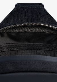 Black fabric bag interior featuring a zippered compartment, textured lining, and a smooth nylon base. Durable, lightweight, and functional design.