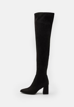 Bottes noires en daim montant jusqu'au genou, avec un bout pointu et un talon bloc, présentant une texture lisse et une silhouette ajustée.