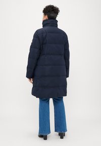 Tumed puffer-jakk kõrge krae ja horisontaalselt tikandatud disainiga, mis on paaritatud helesiniste laienevate teksade ja mustade kontsadega saapatega.