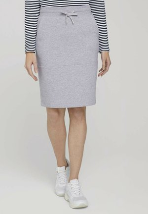 Jupe en jersey gris clair au design ajusté et à taille élastique avec cordon de serrage, associée à des baskets blanches et un haut à rayures noir et blanc à manches longues.