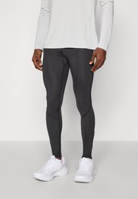Leggings sportivi neri con un design aderente, caratterizzati da dettagli in cucitura e una superficie liscia, abbinati a scarpe da corsa bianche.